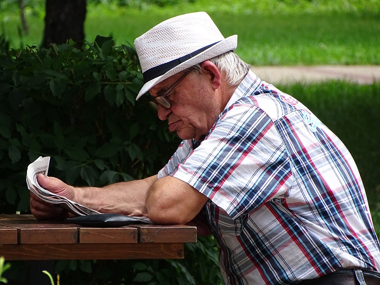 Pessoa idosa aposentada lendo o jornal em um parque