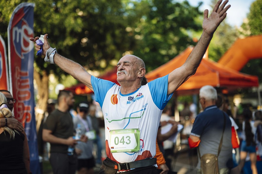 Aposentado comemorando de braços abertos ao completar uma corrida no parque